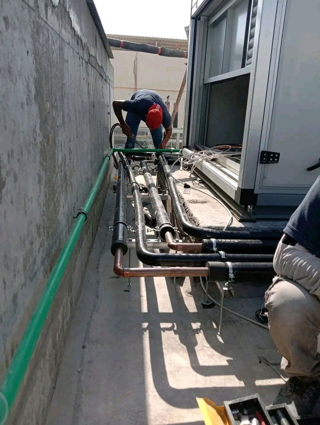 Technicien isolant un réseau de tuyauterie en toiture